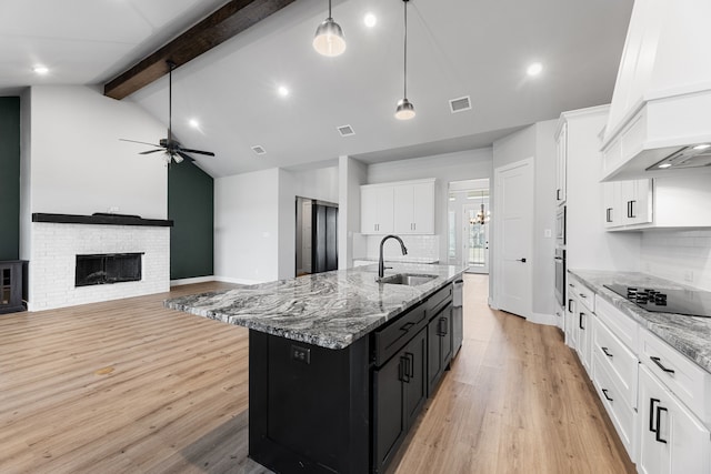 kitchen featuring a center island with sink, a fireplace, visible vents, a sink, and dark cabinets