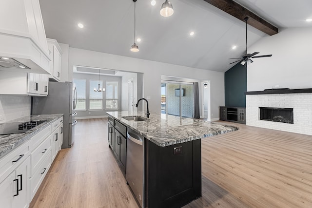 kitchen featuring an island with sink, stainless steel appliances, a brick fireplace, a sink, and ceiling fan with notable chandelier