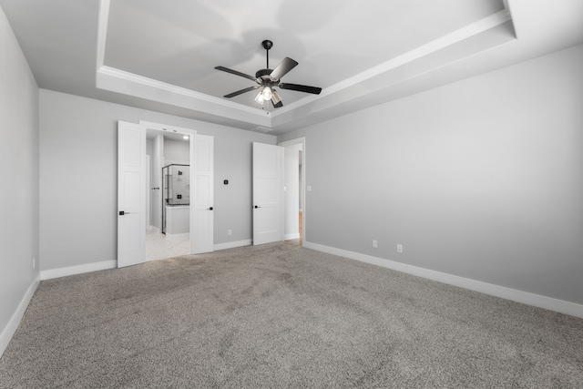 unfurnished bedroom with a raised ceiling, a ceiling fan, light carpet, connected bathroom, and baseboards