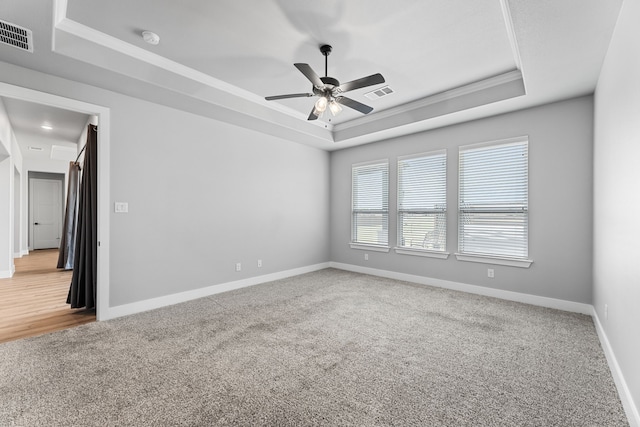 carpeted empty room featuring a tray ceiling and visible vents