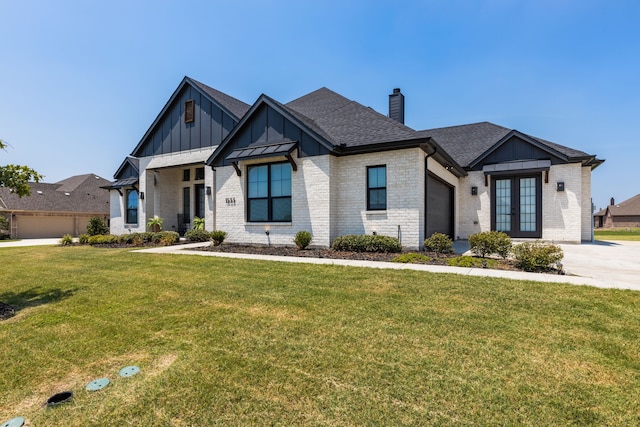 modern inspired farmhouse featuring a shingled roof, french doors, a front yard, board and batten siding, and brick siding