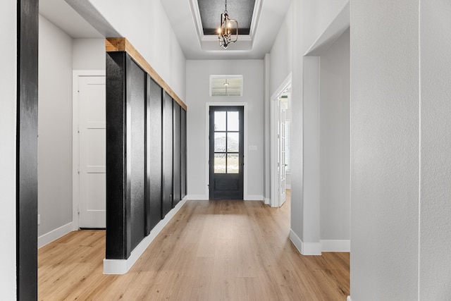 foyer entrance featuring light wood-type flooring, baseboards, a raised ceiling, and a chandelier