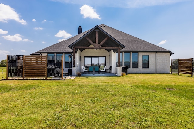 rear view of house with a lawn, a chimney, roof with shingles, fence, and a patio area