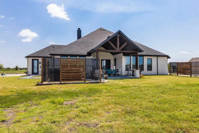 rear view of property featuring a shingled roof, a patio area, a yard, and a chimney