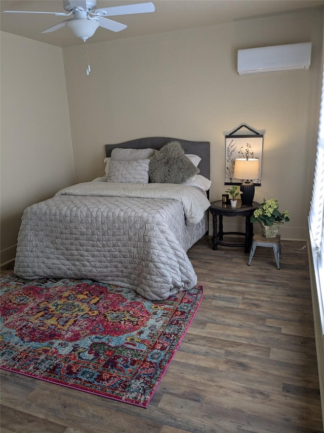 bedroom featuring a ceiling fan, a wall mounted air conditioner, baseboards, and wood finished floors