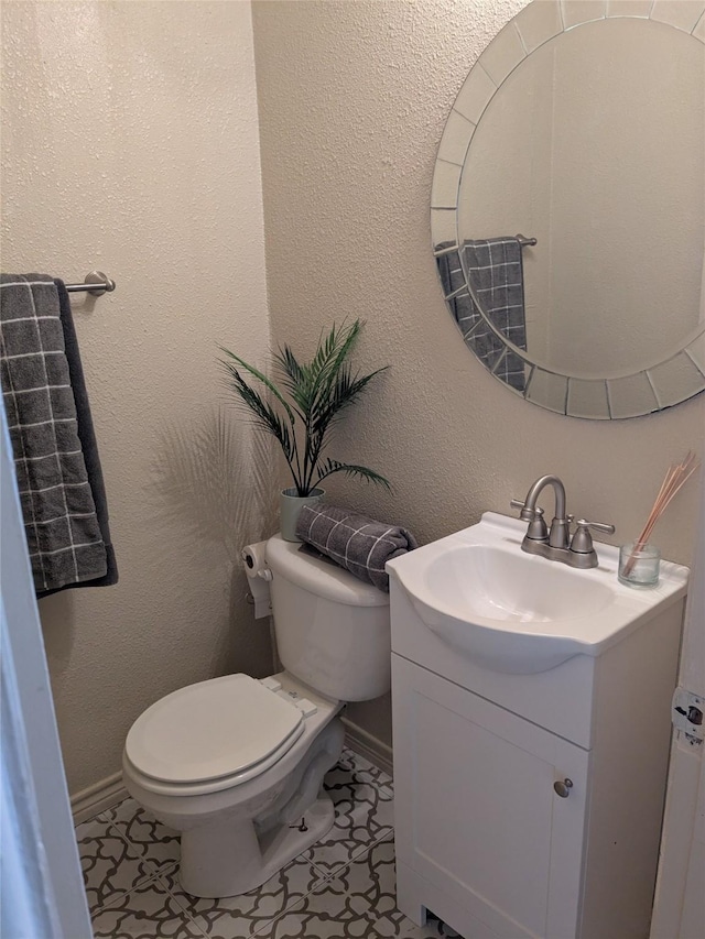 bathroom featuring baseboards, a textured wall, vanity, and toilet