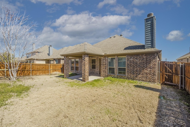 back of property with a patio, brick siding, a chimney, and a fenced backyard