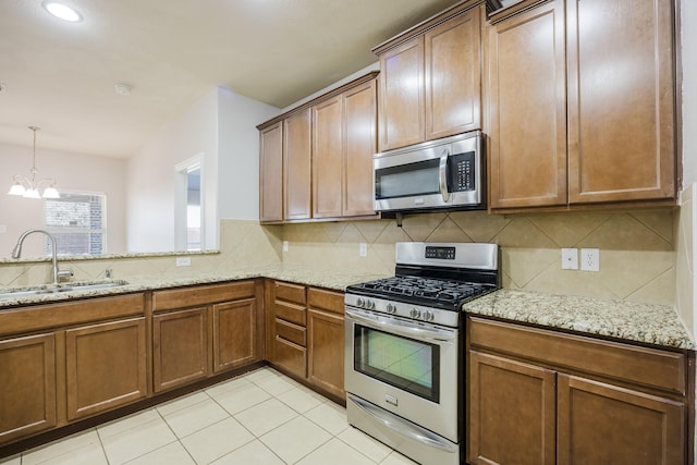 kitchen with stainless steel appliances, light stone counters, a sink, and decorative backsplash