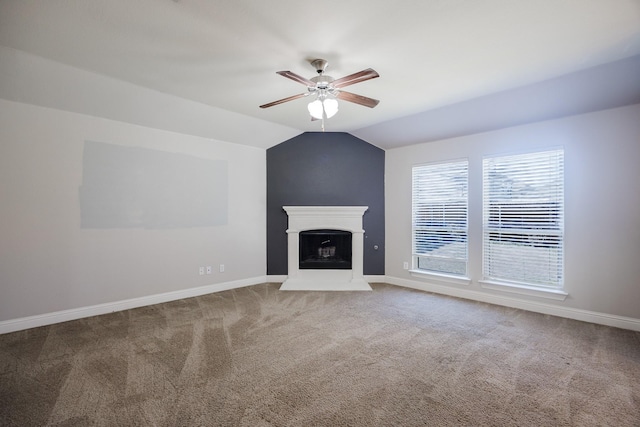 unfurnished living room featuring carpet floors, a fireplace with raised hearth, a ceiling fan, vaulted ceiling, and baseboards