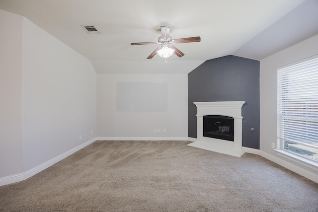 unfurnished living room featuring carpet, a fireplace with raised hearth, visible vents, vaulted ceiling, and ceiling fan