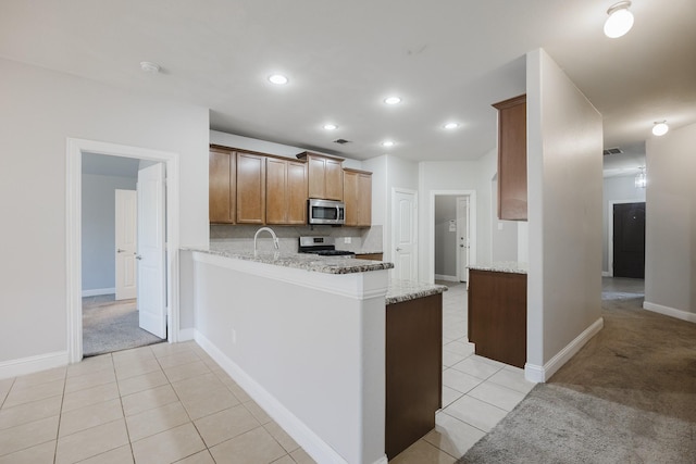 kitchen featuring appliances with stainless steel finishes, a peninsula, light stone counters, and light tile patterned floors