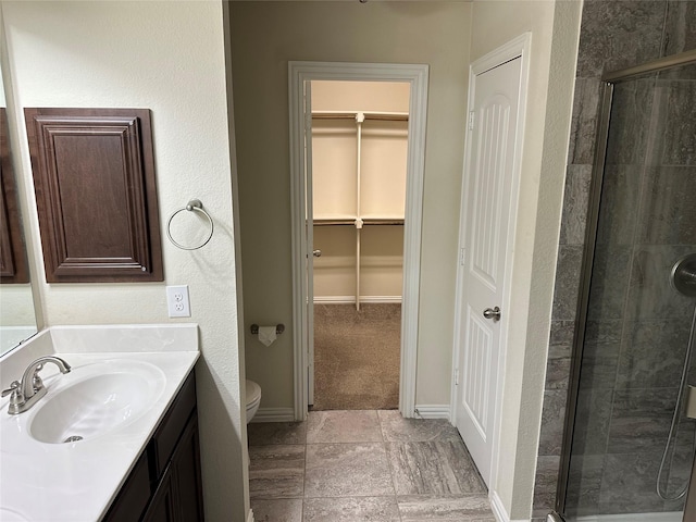 bathroom with a walk in closet, toilet, a shower stall, vanity, and baseboards