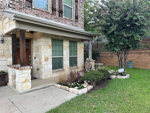 doorway to property with stone siding, brick siding, a lawn, and fence