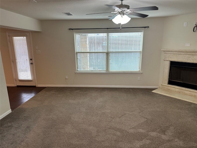 unfurnished living room with dark colored carpet, a glass covered fireplace, and a healthy amount of sunlight