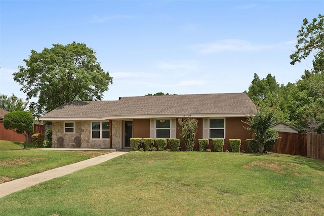 ranch-style home with stone siding, a shingled roof, fence, and a front yard