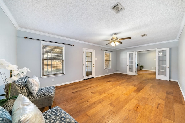 living area featuring visible vents, baseboards, light wood-style flooring, ornamental molding, and french doors