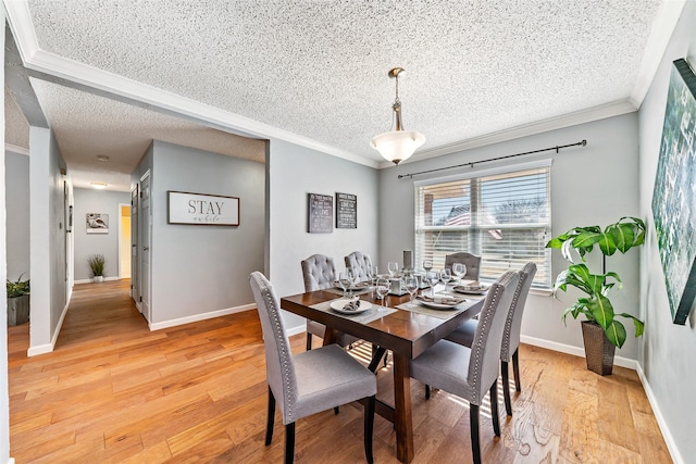 dining room featuring light wood-type flooring, baseboards, ornamental molding, and a textured ceiling