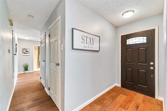 entrance foyer with a textured ceiling, light wood finished floors, and baseboards