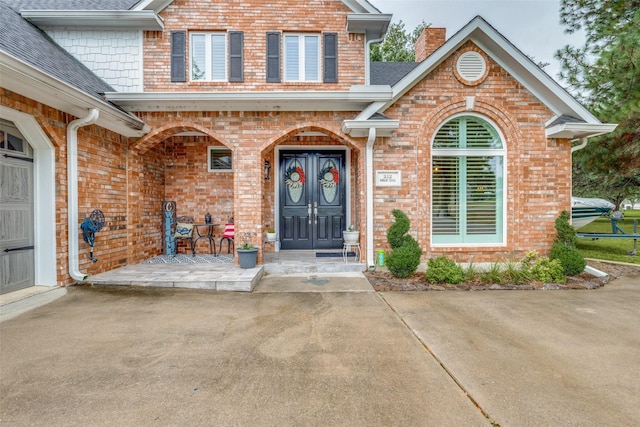 view of exterior entry featuring covered porch, a shingled roof, a chimney, and brick siding