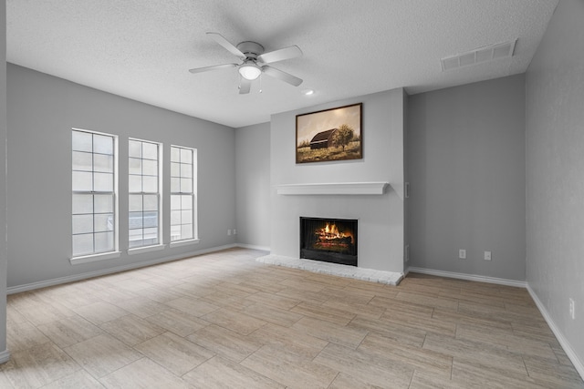 unfurnished living room featuring a warm lit fireplace, baseboards, visible vents, and a ceiling fan