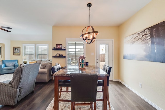 dining area featuring ceiling fan with notable chandelier, dark wood-type flooring, and baseboards