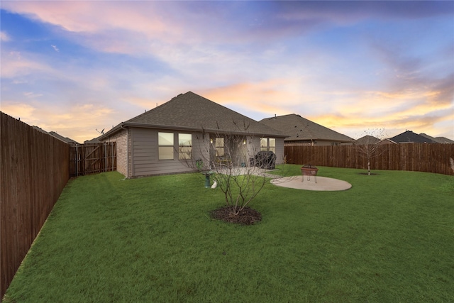 rear view of house featuring a fenced backyard, a shingled roof, a lawn, and a patio