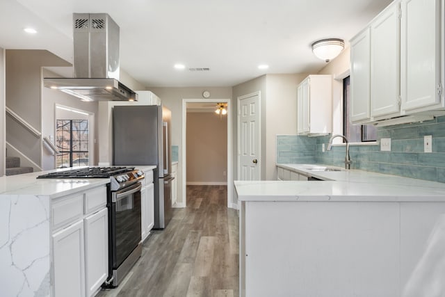 kitchen with a peninsula, island exhaust hood, appliances with stainless steel finishes, and a sink