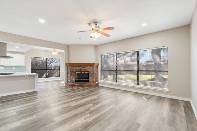 unfurnished living room featuring a ceiling fan, baseboards, light wood finished floors, recessed lighting, and a brick fireplace