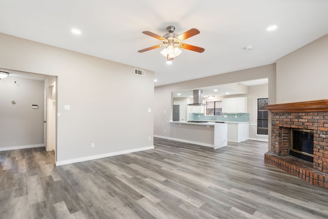 unfurnished living room with a ceiling fan, visible vents, baseboards, a fireplace, and light wood-type flooring