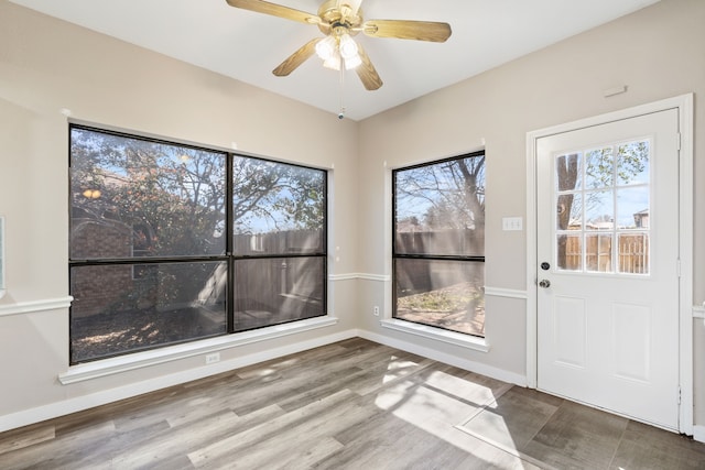 interior space with a ceiling fan, baseboards, and wood finished floors