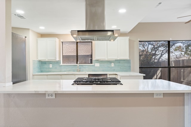 1542 Glenmore Dr, Lewisville, TX 75077 - kitchen featuring island range hood, tasteful backsplash, stainless steel gas cooktop, white cabinets, and light stone countertops