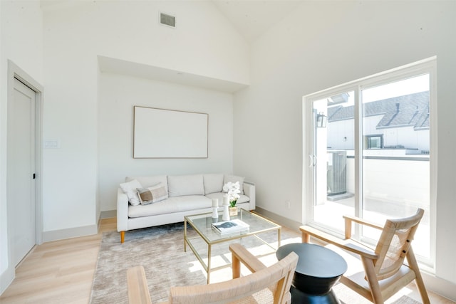 living area featuring light wood-style floors, visible vents, high vaulted ceiling, and baseboards