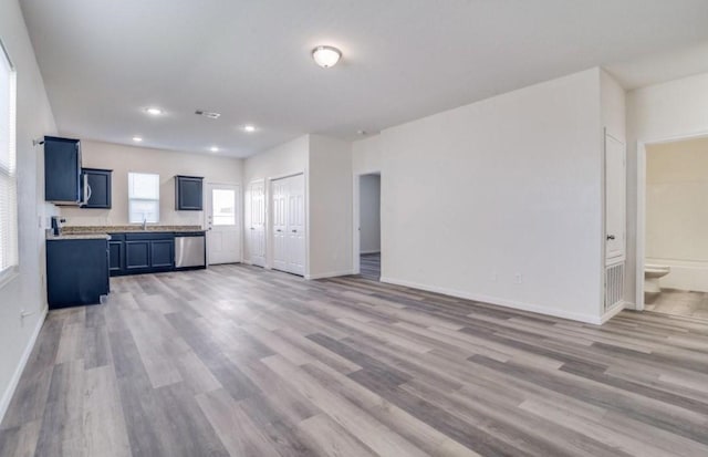 kitchen with stainless steel dishwasher, a sink, blue cabinets, light wood-type flooring, and baseboards