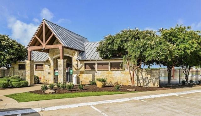 view of front facade featuring stone siding, a standing seam roof, metal roof, and fence