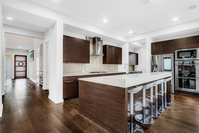 kitchen featuring visible vents, modern cabinets, wall chimney range hood, appliances with stainless steel finishes, and light countertops