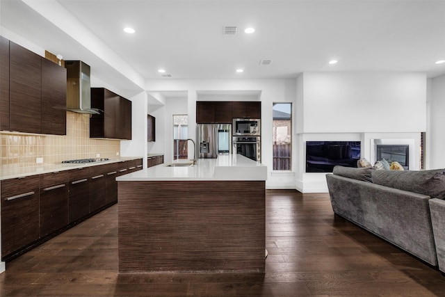 kitchen with modern cabinets, a sink, appliances with stainless steel finishes, wall chimney range hood, and dark wood-style flooring