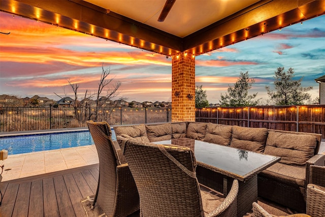 pool at dusk with outdoor lounge area, a fenced backyard, a fenced in pool, and ceiling fan