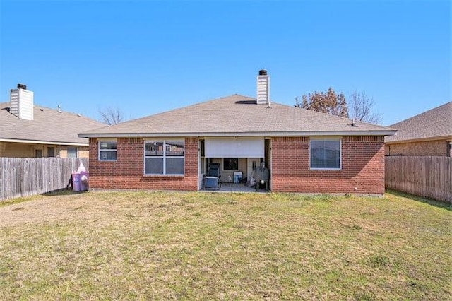 back of property with a fenced backyard, a lawn, a chimney, and brick siding