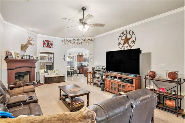 living area with arched walkways, light colored carpet, a fireplace, a ceiling fan, and ornamental molding