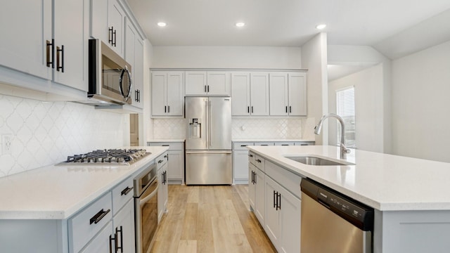 kitchen featuring light wood-style flooring, a center island with sink, a sink, stainless steel appliances, and light countertops