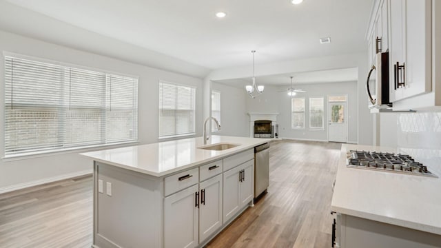 kitchen featuring a fireplace, stainless steel appliances, a sink, light wood-style floors, and open floor plan