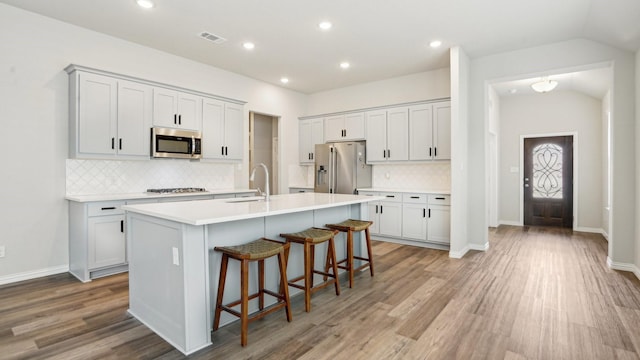 kitchen with a breakfast bar area, lofted ceiling, an island with sink, a sink, and stainless steel appliances