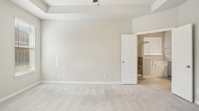 unfurnished bedroom with light colored carpet, a raised ceiling, and baseboards