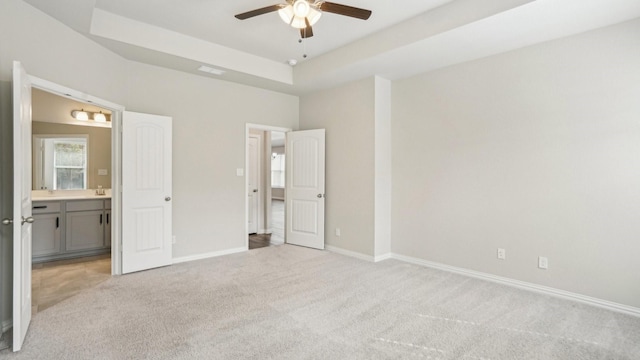 unfurnished bedroom with visible vents, light carpet, a raised ceiling, ensuite bathroom, and baseboards