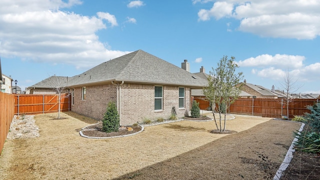 rear view of house featuring brick siding, a shingled roof, and a fenced backyard