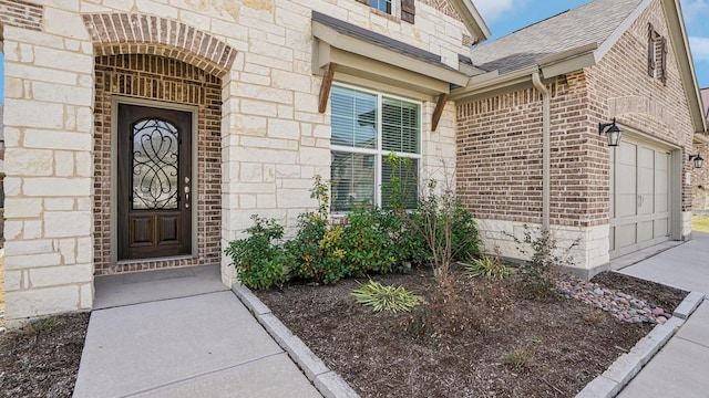 property entrance featuring brick siding, an attached garage, driveway, and roof with shingles