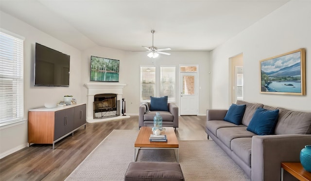 living room featuring wood finished floors, baseboards, a ceiling fan, vaulted ceiling, and a glass covered fireplace