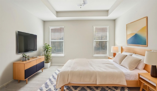 bedroom featuring visible vents, light colored carpet, a tray ceiling, and baseboards