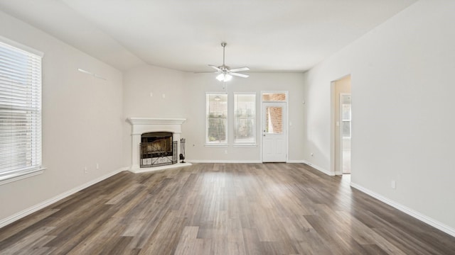 unfurnished living room with dark wood-type flooring, a fireplace with raised hearth, baseboards, and ceiling fan