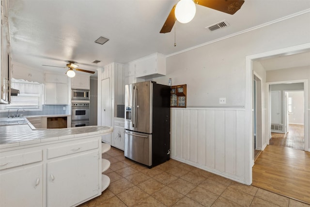 kitchen with visible vents, a wainscoted wall, tile countertops, appliances with stainless steel finishes, and white cabinets